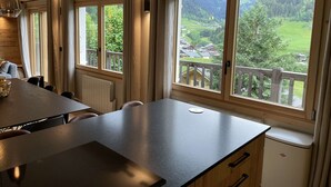 A modern kitchen with a large island, wooden cabinets, and a view of a green landscape through large windows. - Contemporary chalet for 8, 4 bedrooms, mountain views, parking, near village (Arêches-Beaufort)