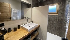 Un baño moderno con tocador de madera, un espejo grande, cabina de ducha y una ventana pequeña.