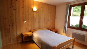 Een slaapkamer met een houten bed, nachtkastjes, een wandlamp, een raam met gordijnen en een radiator.