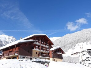 A chalet-style building with multiple balconies and a ski slope in the background.
