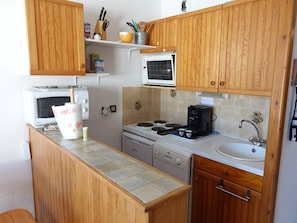 A compact kitchen with wooden cabinets, a microwave, a stove, a coffee maker, and a sink.