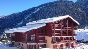 Een chalet met twee verdiepingen en een balkon, omgeven door met sneeuw bedekte bergen.
