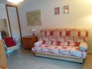 A cozy living room with a sofa, a small wooden cabinet, a chair, and a mirror.