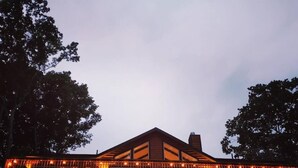 A modern building with a sloped roof and large windows, surrounded by trees.