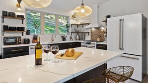 A modern kitchen with a large island, white appliances, and pendant lighting.