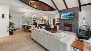 A spacious living room with a fireplace, a dining area, and a kitchen in the background.