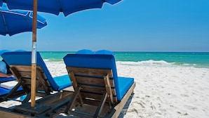 A beach with wooden lounge chairs and blue umbrellas.