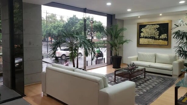 A modern living room with a white sofa, a coffee table, and a large window offering a view of the street.