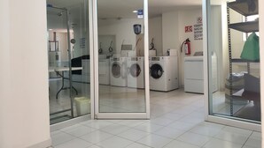 A laundry room with glass doors, multiple washing machines, a fire extinguisher, and a water heater.