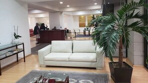 A modern lobby with a reception desk, a white sofa, a coffee table, and a large potted plant.