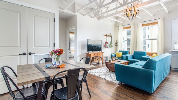 A spacious living room with a wooden dining table, blue sofa, and a television. - Speakeasy & Pool · 2BR Sleeps 6 · Dog-Friendly (Nashville)
