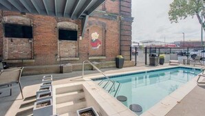 An outdoor swimming pool with a brick wall and a mural, surrounded by lounge chairs and a covered seating area. - Speakeasy & Pool · 2BR Sleeps 6 · Dog-Friendly (Nashville)