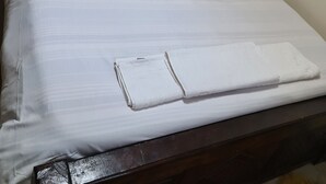 Ein ordentlich bezogenes Bett mit weißen Leinen und Kissen, ein Holz-Kopfteil mit geometrischem Muster und ein gefaltetes weißes Handtuch auf dem Bett.