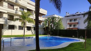 A swimming pool surrounded by a well-maintained lawn, with a modern building in the background. - COSTA DE LA LUZ APARTMENT (Rota)
