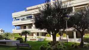A modern building with a flat roof, multiple balconies, and a well-maintained garden with benches and a lamp post. - COSTA DE LA LUZ APARTMENT (Rota)