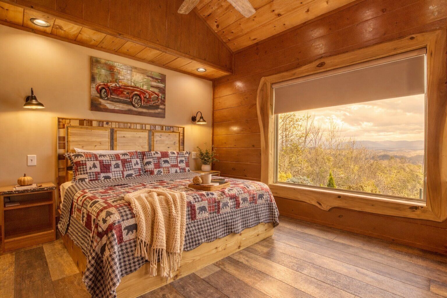 A cozy bedroom with a large bed, wooden walls, a window with a view, and a painting on the wall.