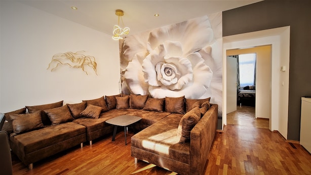 A modern living room with a large sectional sofa, a small coffee table, and a wall mural of a large flower. - Vienna CityApartments - Luxury 2 (Vienna)