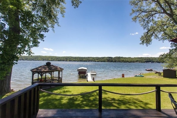 A lakeside view from a deck with a gazebo, dock, and small docked boat.