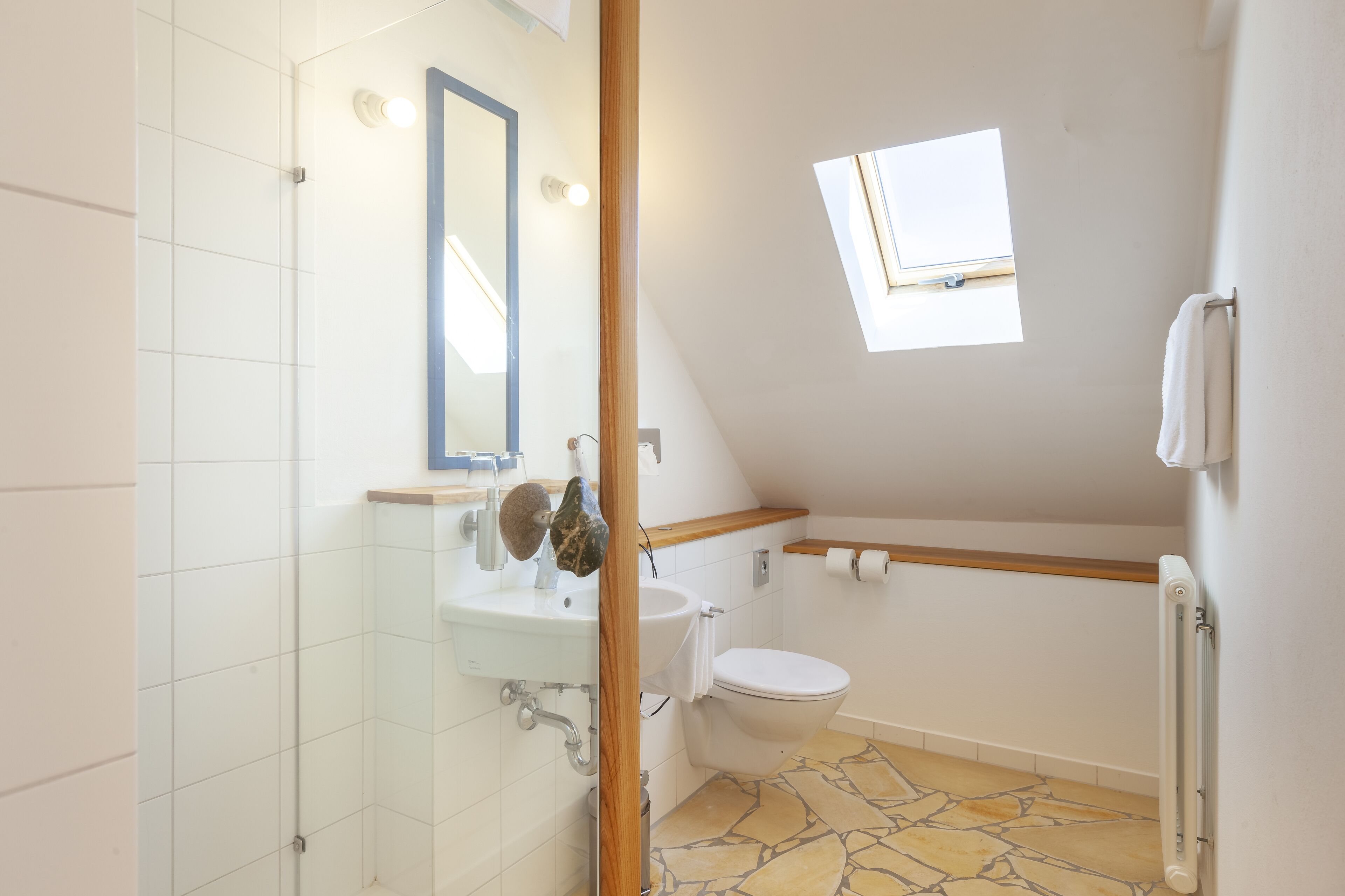 A bathroom with a stone-tiled floor, a white sink, a toilet, and a skylight.
