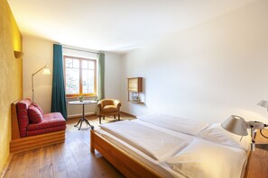 A room with a bed, a sofa, a chair, a lamp, a window, and a radiator. - Alter Wirt GmbH in Grünwald (Gruenwald)