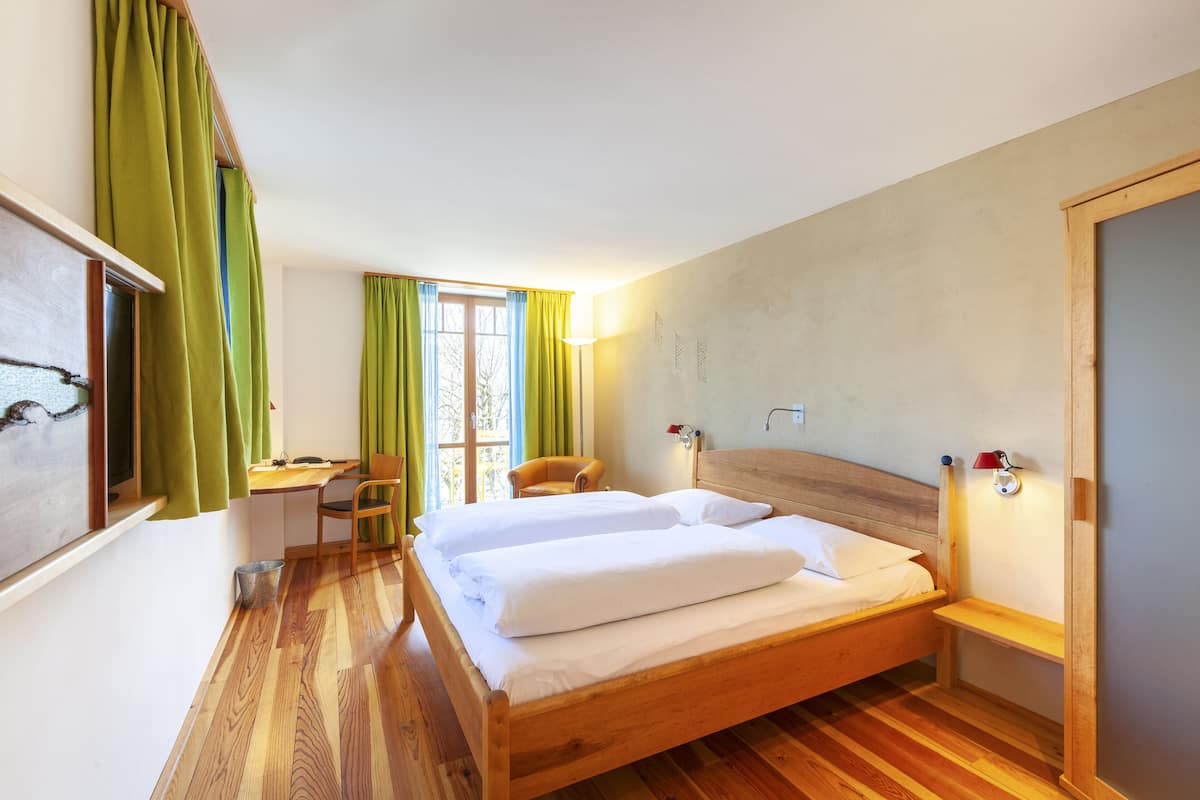 A room with a wooden bed, a desk, a chair, and a window with curtains.