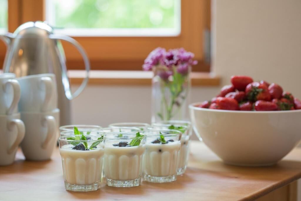 Uma mesa com vários copos de uma bebida cremosa, adornada com hortelã, uma jarra e uma tigela de morangos.