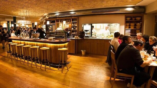 A restaurant with a bar area, wooden flooring, and patrons dining.