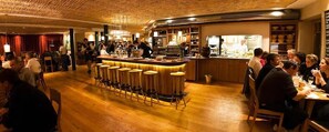 A restaurant with a bar area, wooden flooring, and patrons dining. - Alter Wirt GmbH in Grünwald (Gruenwald)