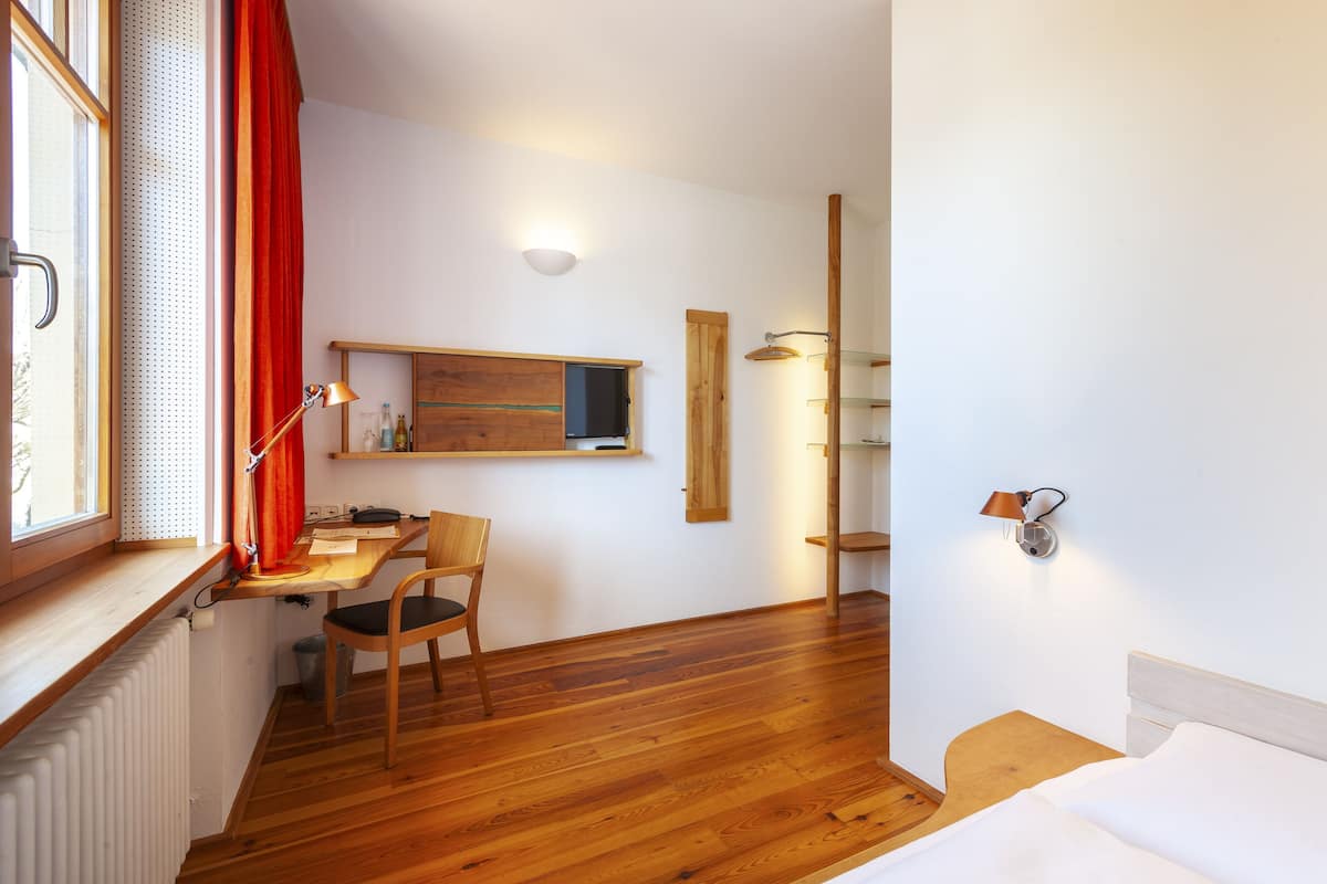 A room with a wooden desk, chair, bed, and a window with curtains.