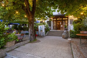 An outdoor café area with tables and chairs, a stone pathway, and a building entrance with steps. - Alter Wirt GmbH in Grünwald (Gruenwald)