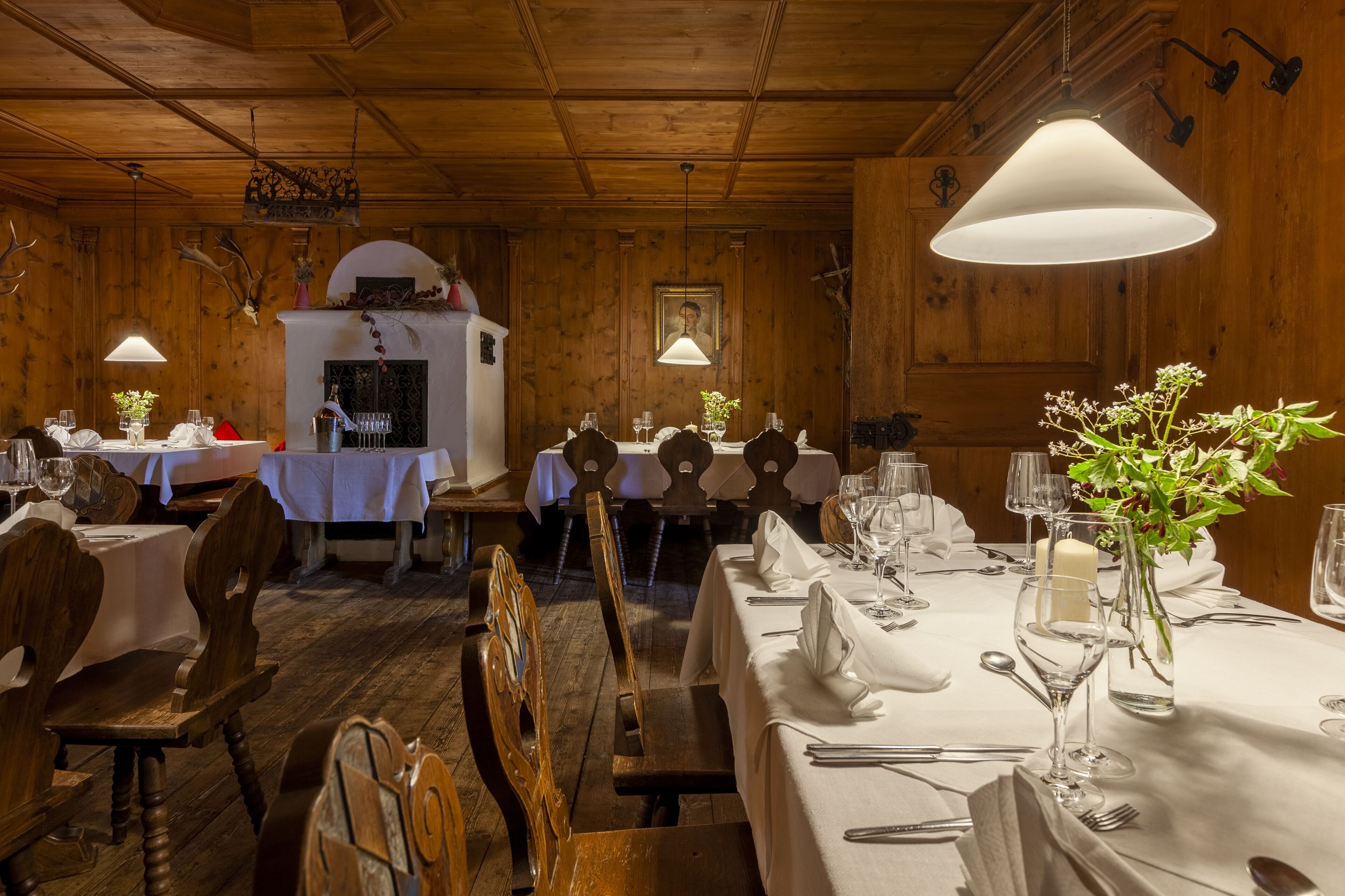 A wooden interior with tables set for dining, white tablecloths, and hanging pendant lights.