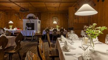 A wooden interior with tables set for dining, white tablecloths, and hanging pendant lights.