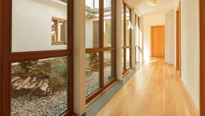 A hallway with large windows, wooden flooring, and a view of an outdoor garden area.