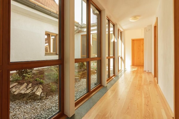 Un couloir doté de grandes fenêtres, d’un plancher en bois et offrant une vue sur un jardin extérieur.