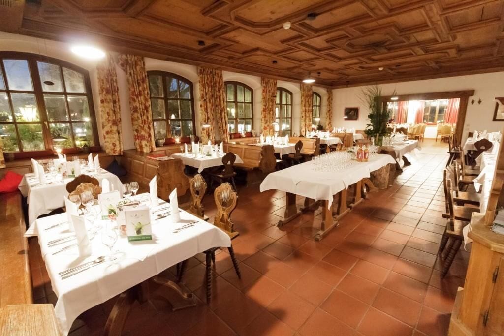 A restaurant with multiple tables set for dining, wooden ceiling, large windows, and a view of the outdoors.