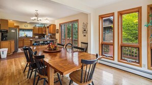 A spacious kitchen with wooden cabinets, a large dining table, and a view of the outdoors through large windows.