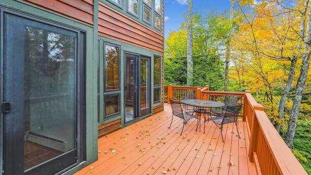 A wooden deck with a table and chairs, surrounded by autumn foliage.