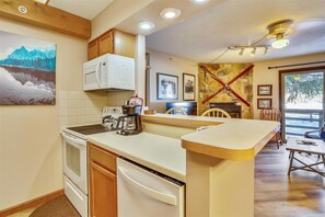 Compact kitchen with stove, microwave, and dishwasher, plus a dining area with a wooden table and chairs.