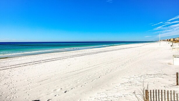 Une vaste plage de sable fin, avec une eau d’un bleu limpide et un ciel dégagé.
