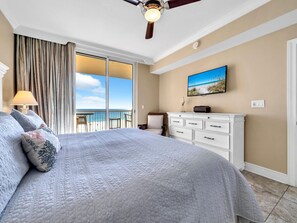 Un dormitorio con una cama grande, ventilador de techo, vista a la playa, cómoda y lámpara.