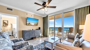 Un salón amplio con un sofá grande, una mesa de centro y un televisor. Hay un balcón con vista a la playa.