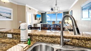 Una cocina de hotel con encimeras de granito, un lavamanos de acero inoxidable y un comedor con vista al océano.