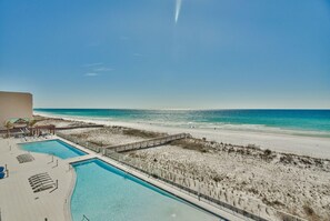 A pool area with a beach view, a wooden deck, and a sandy beach.