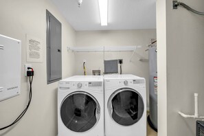 A laundry room with two front-loading washing machines, a Siemens electrical panel, a water heater, and a ceiling-mounted security camera. - Heron 303-HUGE CORNER CONDO w/ Wrap Around Balcony overlooking Lazy River & Bay! (Fort Walton Beach)