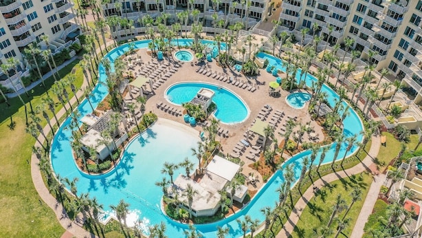 Eine Luftaufnahme eines Resorts mit mehreren Swimmingpools, Palmen und Liegestühlen.