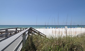 A wooden boardwalk leading to a beach with blue umbrellas and a clear sky.