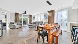 A spacious living area with a dining table set for four, a sofa, and a balcony with curtains.
