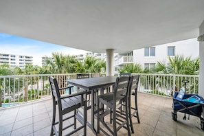 Un balcon avec une table et des chaises, une poussette, et une vue sur des palmiers et des immeubles.