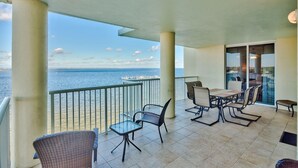 A balcony with a view of the sea, featuring a table and chairs, and a glass door leading inside.