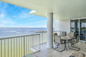 Un balcón con vista al mar, una mesa con sillas y una puerta de vidrio que da a un espacio interior.